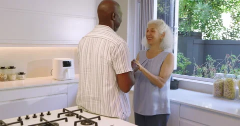 Diverse couple clasping hands in kitchen at gas cooktop leaning in for kiss and Stock Footage 311022818