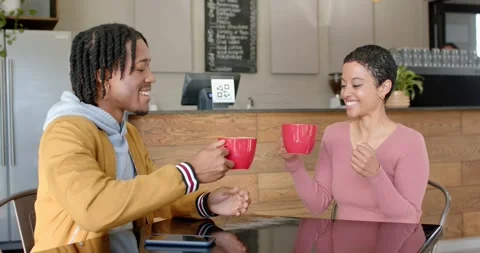 Diverse couple clinking red mugs sharing talk over coffee across cafe table Vídeo Stock 336437259