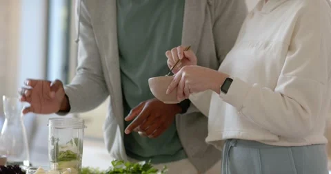 Diverse couple cooking, man opening jar and offering spoon, woman stirring bowl Stock Footage 345589800