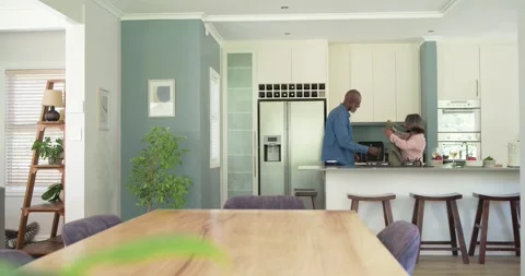 Diverse couple dancing in kitchen, man reaching across island taking woman's Stock Footage 345063766