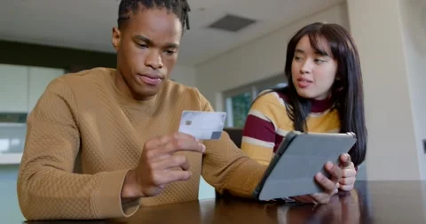 Diverse couple at dining table, man showing payment card to tablet folio case to Stock Footage 344774367