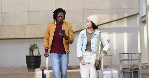 Diverse couple entering frame walking beside building pulling suitcases checking Vídeos de archivo 317809066