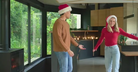 Diverse couple entering kitchen wearing Santa hats dancing near candlelit island Stock Footage 337932854