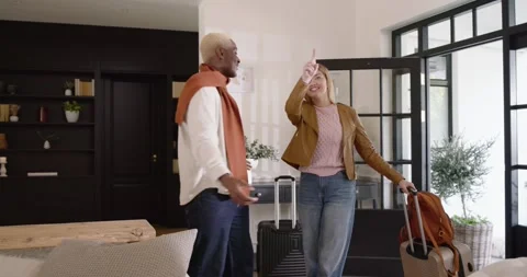 Diverse couple entering through open glass front door, pulling suitcases, Stock Footage 344679074