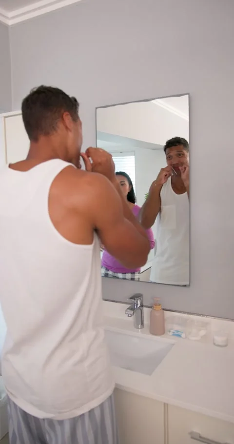 Diverse couple flossing at bathroom sink while woman showing smartphone, pausing Stock Footage 345319846