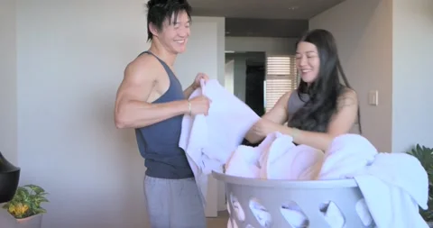 Diverse couple folding white towels and linens on bed, prompted by full grey Stock Footage 335365892