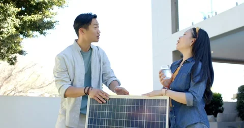 Diverse couple holding solar panel on porch, man pointing adjusting toward Video stock 337933001