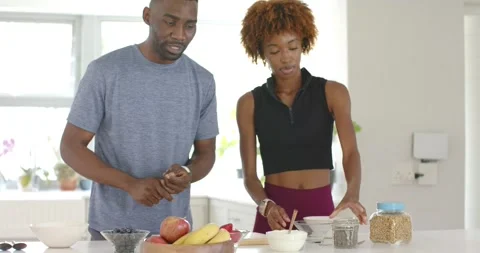 Diverse couple in kitchen, gray tee man gesturing, woman in black crop topping Stock Footage 335986916