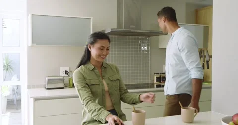 Diverse couple at kitchen island with man entering with mug stirring sugar and Vídeo Stock 340986221