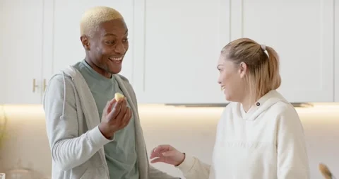 Diverse couple in kitchen offering bite, feeding, preparing pineapple smoothie Stock Footage 345589764