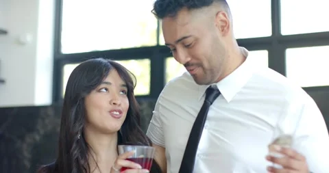 Diverse couple in kitchen by window, wearing formal, woman raising glass Stock Footage 341937877