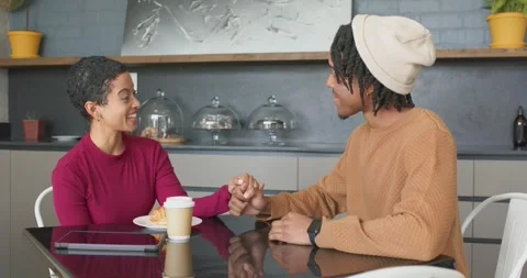 Diverse couple laughing at modern cafe, reaching, grasping hands over coffee cup Vídeo Stock 340964348