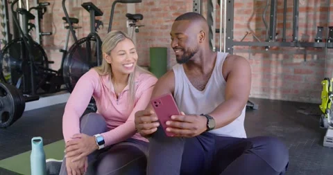 Diverse couple laughing while man extending pink-cased smartphone, showing Stock Footage 342023570