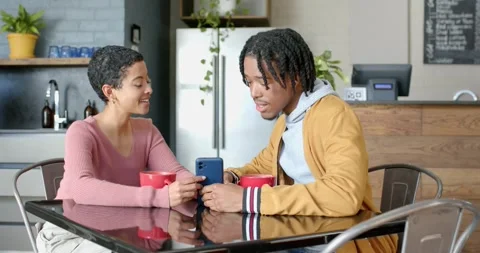 Diverse couple leaning at glass kitchen table noticing smartphone screen Stock Footage 335808628