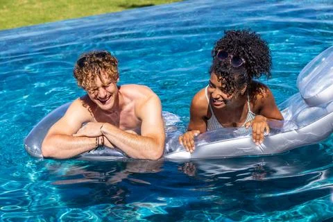 Diverse couple leaning on silver float in home pool shirtless man woman wearing Stock Photos