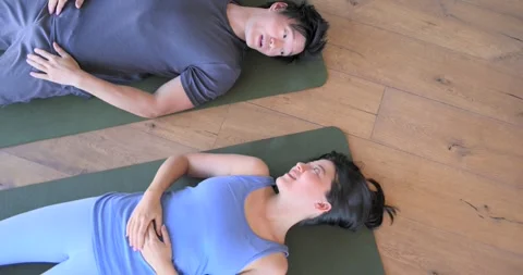 Diverse couple lying on green mats in room, man extending arm and woman meeting 스톡 동영상 337540679