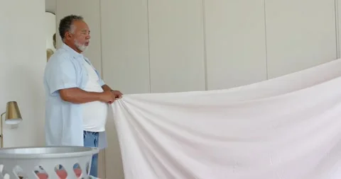 Diverse couple with man pulling pink bedsheet taut, woman joining, stretching Stock Footage 335269466