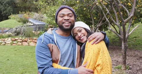 Diverse couple noticing camera in garden, embracing and smiling warmly to Stock Footage 340256917