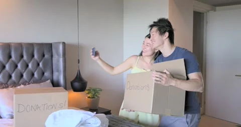Diverse couple packing donations into boxes labeled Donations in bedroom, taking Stock Footage 340393802