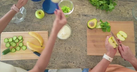 Diverse couple placing apple, slicing and adding cucumber into blender for Stock Footage 335269061