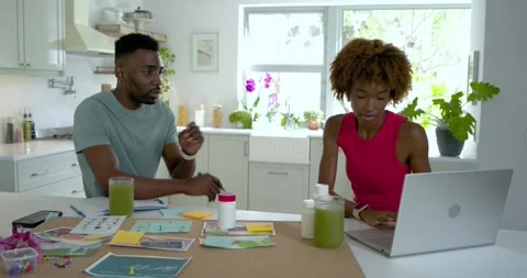 Diverse couple planning at kitchen island with laptop, woman holding bottle Stock Footage 339651718