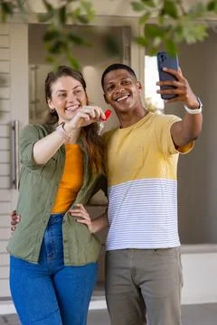 Diverse couple posing, taking selfie with smartphone at house entrance while Fotos Stock