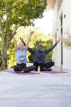 Diverse couple practicing stretch on concrete patio by house with purple mats Fotos Stock