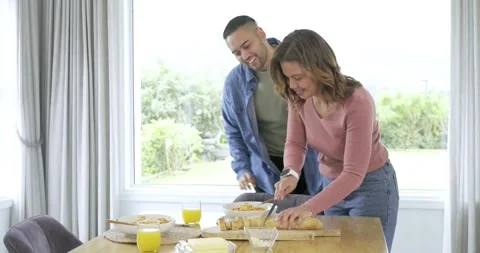 Diverse couple preparing breakfast at home slicing bread embracing twirling Stock Footage 336366991