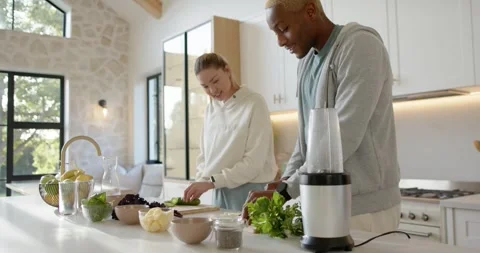 Diverse couple preparing meal at kitchen island, slicing cucumber, chopping Stock Footage 345589735