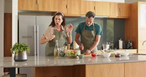 Diverse couple preparing salad in home kitchen, woman guiding while man chopping Stock Footage 341736632