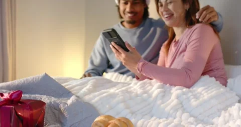 Diverse couple pressing remote for show scrolling phone sending greetings over Vídeo Stock 344225693