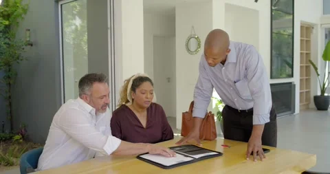 Diverse couple prompted by papers, advisor leaning in, pointing to folder at Stock Footage 341242225