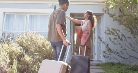 Diverse couple pulling luggage walking along path to enter home, woman showing Stock Footage 341241520