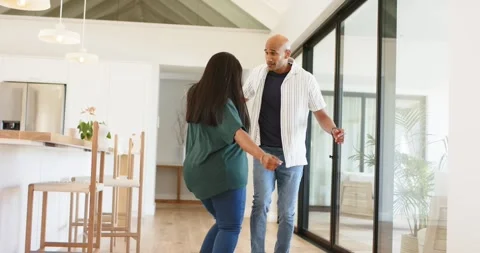 Diverse couple reaching hands and dancing at kitchen island, spinning into solo, Stock Footage 338325838