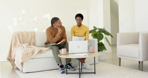 Diverse couple reading document, reviewing finances on laptop, jotting notes at Video stock 313231265