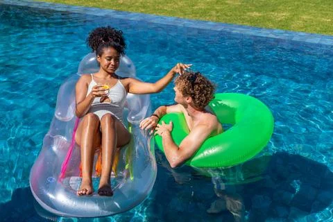 Diverse couple reclining on clear float and green ring in pool, wearing swimsuit Fotos Stock