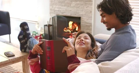 Diverse couple reclining on sofa holding red hardcover book and pointing pages Stock Footage 344253476