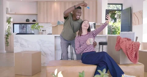 Diverse couple recording move-in selfie at home, woman holding phone, mug, man Stock Footage 337730103