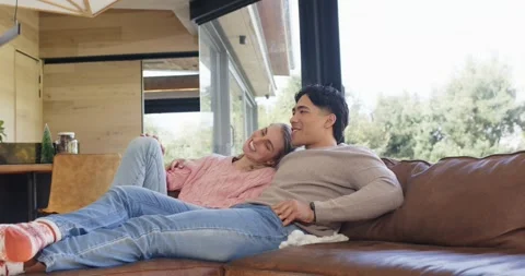 Diverse couple settling on couch while woman lifting head chatting about view Stock Footage 340964289
