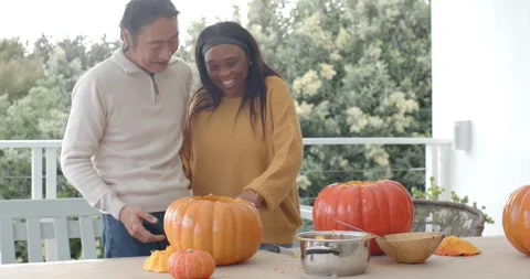 Diverse couple sharing affectionate moment then scooping and carving pumpkins on Video stock 346179599