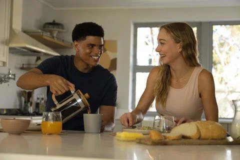 Diverse couple sharing breakfast at kitchen island, man pouring French press Stock Photos