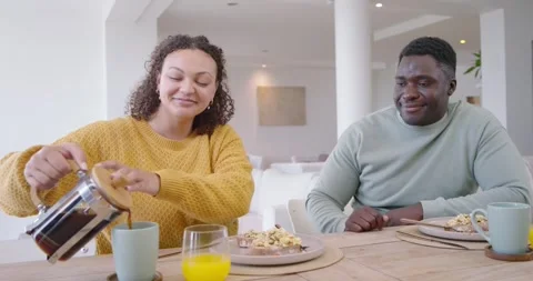 Diverse couple sharing breakfast at table, woman reaching for press, pouring Stock Footage 339231746