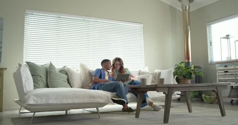 Diverse couple sitting on couch, man pointing tablet, woman adjusting tablet, Stock Footage 341851842