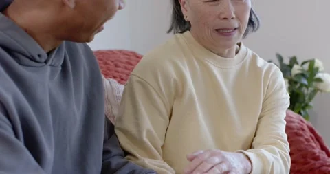 Diverse couple sitting on couch, man speaking while senior Asian woman holding Stock Footage 345509085