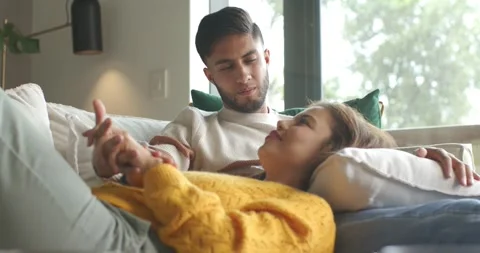 Diverse couple sitting on couch by window, man holding hands, speaking softly Stock Footage 337886286