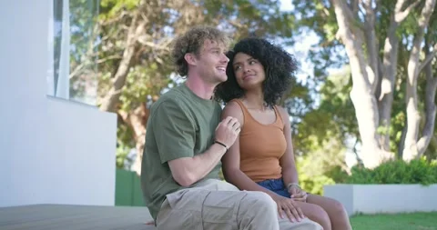 Diverse couple sitting on deck by glass railing man talking leaning in touching Video stock 334924941
