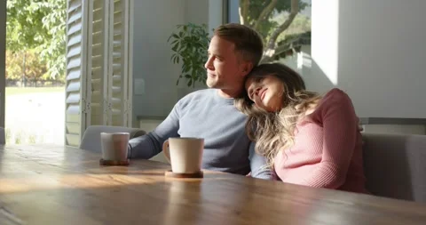 Diverse couple sitting at dining table, woman leaning on man's shoulder, sun Stock Footage 345072661