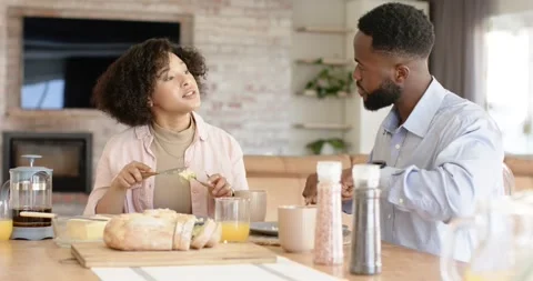 Diverse couple sitting at kitchen table sipping coffee and cutting scrambled Stock Footage 340964085