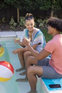 Diverse couple sitting poolside in backyard, wearing cover-up and pink tee, Fotos de archivo