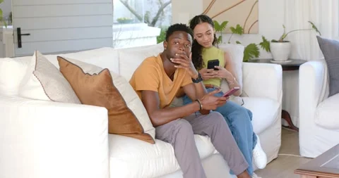 Diverse couple sitting on white sofa, man rubbing forehead while both comparing Stock Footage 338326536